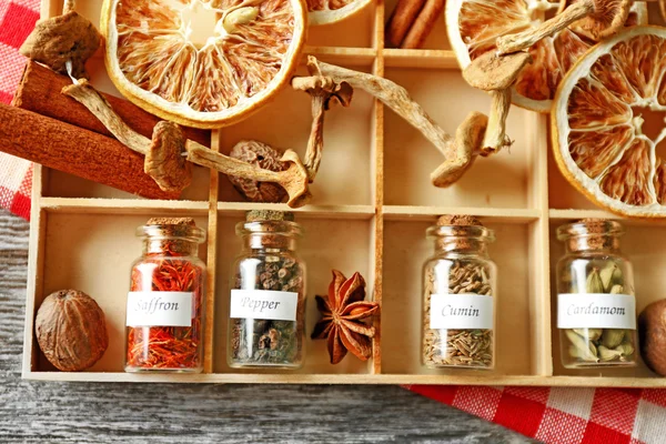 Assortment of spices in glass bottles in box, on wooden background — Stock Photo, Image