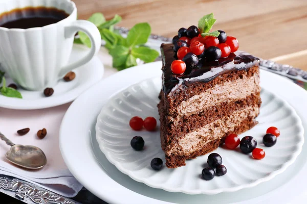 Delicioso bolo de chocolate com bagas e xícara de café na mesa de perto — Fotografia de Stock