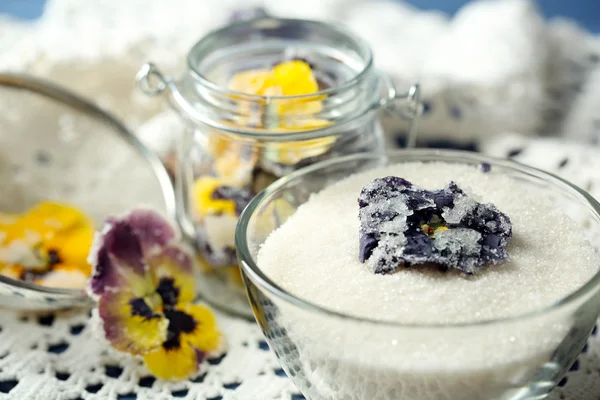 Candied sugared violet flowers, in glass jar and bowl, on wooden background — Stock Photo, Image