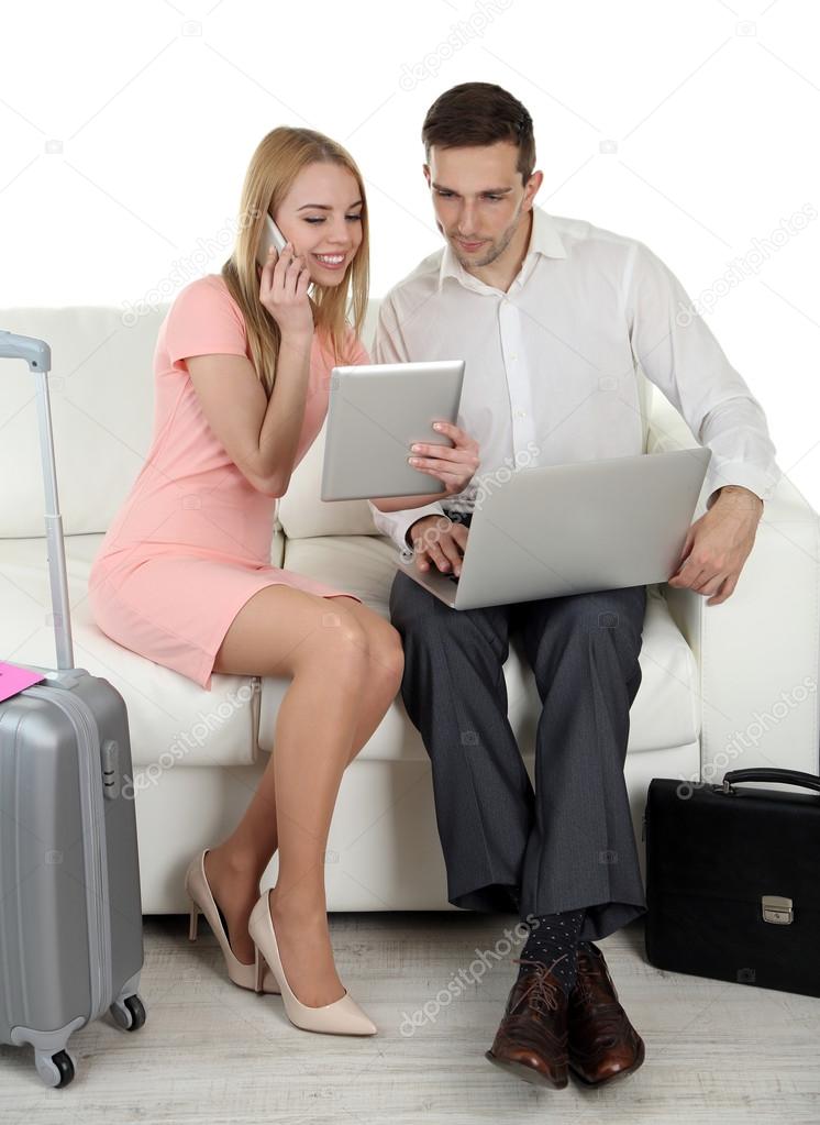 Portrait of young happy couple with baggage, digital tablet and laptop sitting on sofa. Isolated on white