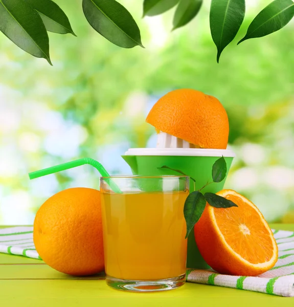 Citrus press, glass of juice and ripe oranges on nature background — Stock Photo, Image