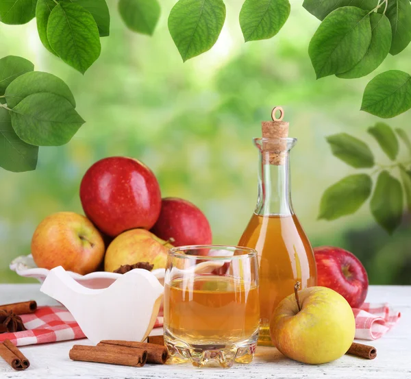 Sidra de manzana en botella con palitos de canela y manzanas frescas sobre fondo natural — Foto de Stock