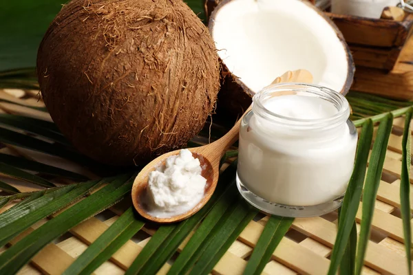 Coconut with leaf and cosmetic cream in jar on wooden background — Stock Photo, Image