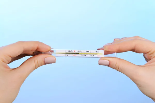 Manos femeninas sujetando el termómetro sobre fondo azul — Foto de Stock