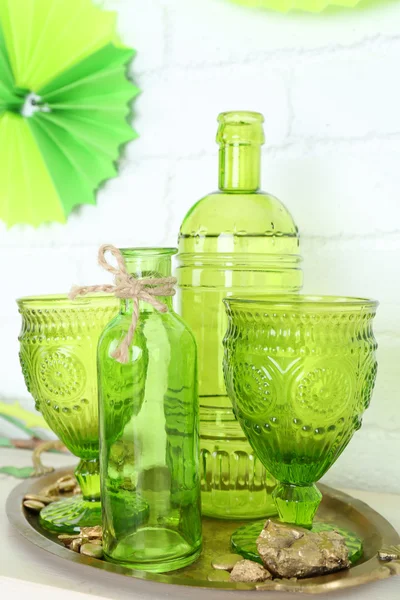 Bicchieri verdi e bottiglie sul tavolo su sfondo muro di mattoni — Foto Stock