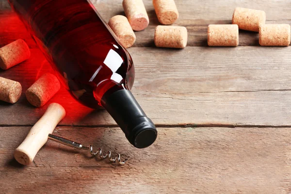 Glass bottle of wine with corks and corkscrew on wooden table background — Stock Photo, Image