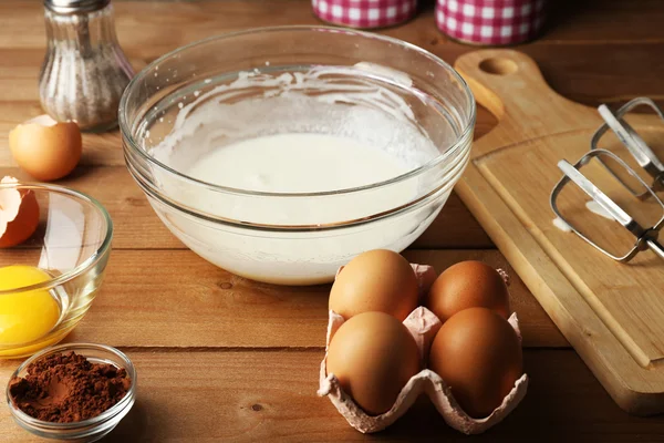 Preparation cream with eggs in glass bowl on wooden background — Stock Photo, Image