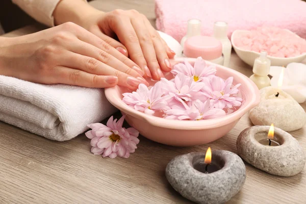 Mains féminines et bol d'eau de spa avec des fleurs, gros plan — Photo