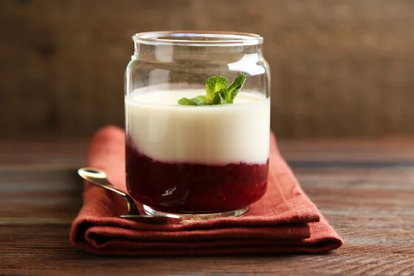 Tarro de vidrio con sabroso postre de panna cotta en plato, sobre mesa de madera —  Fotos de Stock