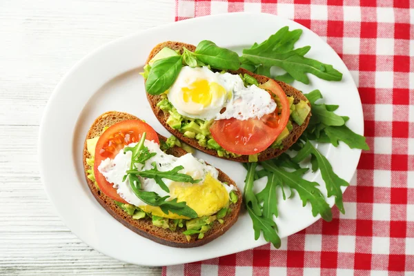 Sabrosos sándwiches con huevo, aguacate y verduras en plato, sobre fondo de madera — Foto de Stock