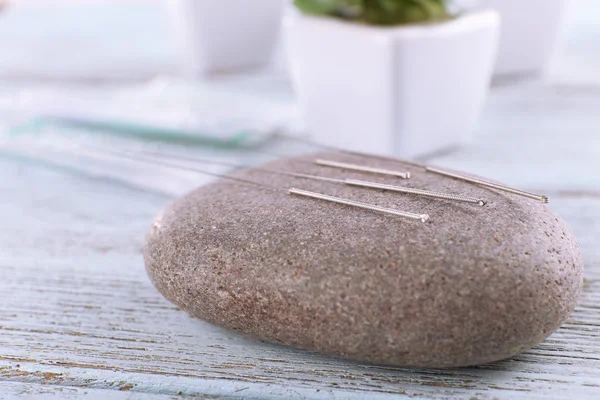 Agujas de acupuntura con piedra spa sobre mesa de madera, primer plano —  Fotos de Stock