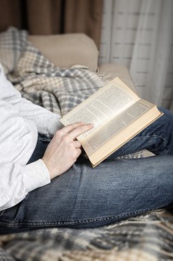 Young man reading book, close-up, on home interior background clipart