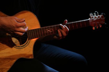 Genç adam akustik gitarla çalıyor.