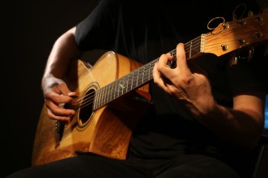 Genç adam akustik gitarla çalıyor.
