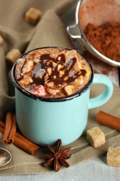 Cup of hot coffee with marshmallow on fabric with lump sugar, cinnamon, star anise and stainer of cocoa on color wooden planks background — Stock Photo, Image