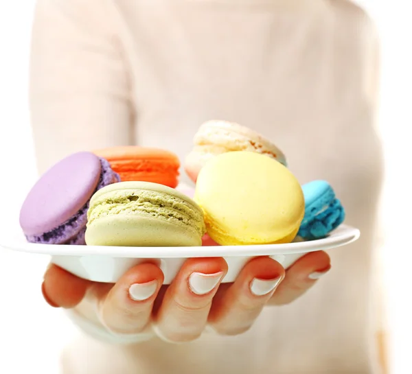 Tallrik med läckra färgglada macaroons i kvinnlig hand på vit bakgrund — Stockfoto