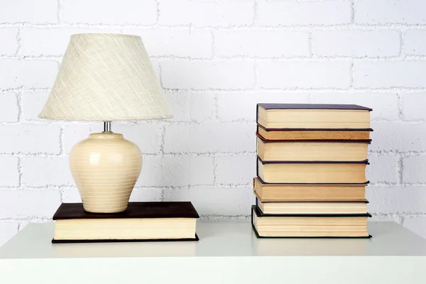 Prateleira de madeira com livros e lâmpada no fundo da parede de tijolo — Fotografia de Stock