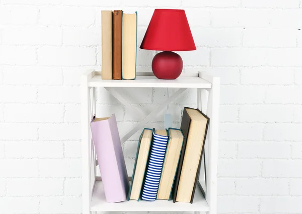 Wooden shelf with books and lamp on brick wall background — Stock Photo, Image