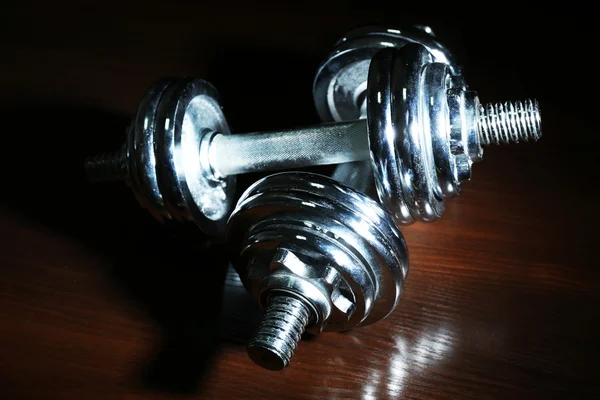 Dumbbells on wooden floor, on dark background — Stock Photo, Image