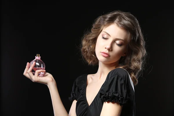 Hermosa mujer con frasco de perfume sobre fondo negro — Foto de Stock