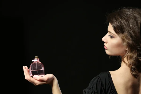 Hermosa mujer con frasco de perfume sobre fondo negro —  Fotos de Stock