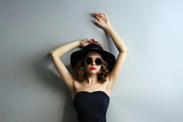 Retrato de modelo hermoso en vestido negro, sombrero y gafas de sol sobre fondo gris —  Fotos de Stock