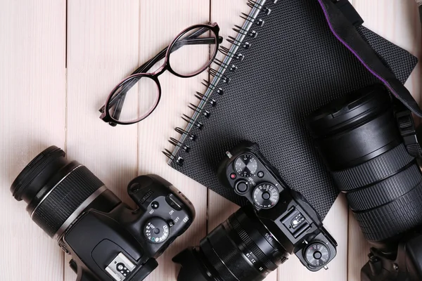 Câmeras modernas com óculos e notebook em mesa de madeira, vista superior — Fotografia de Stock