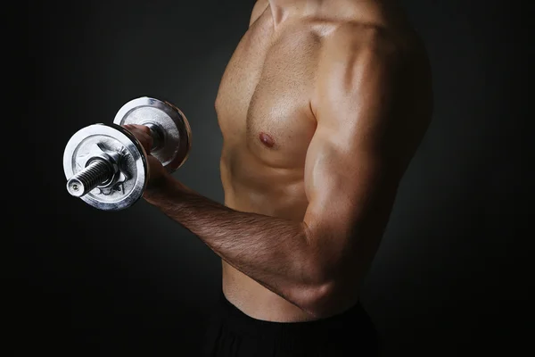 Muscolo giovane uomo in possesso di manubri su sfondo scuro — Foto Stock