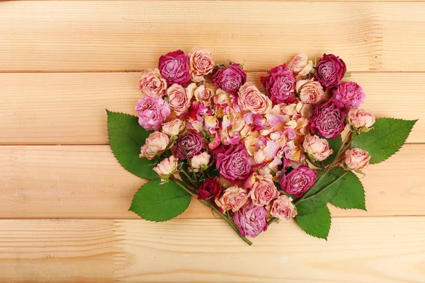 Cuore di bei fiori secchi e foglie verdi su sfondo di legno — Foto Stock