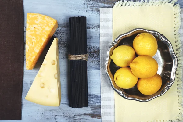 Queso, espaguetis negros y limones en vista de mesa de madera — Foto de Stock