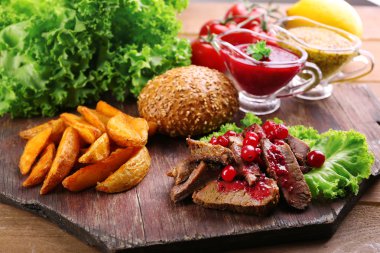 Kızılcık sosu, kavrulmuş patates dilimleri ve ahşap arka plan üzerinde kesme tahtası üzerinde topuz ile sığır eti