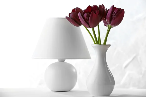Красивый фиолетовый тюльпан в вазе с лампой на светлом фоне — стоковое фото