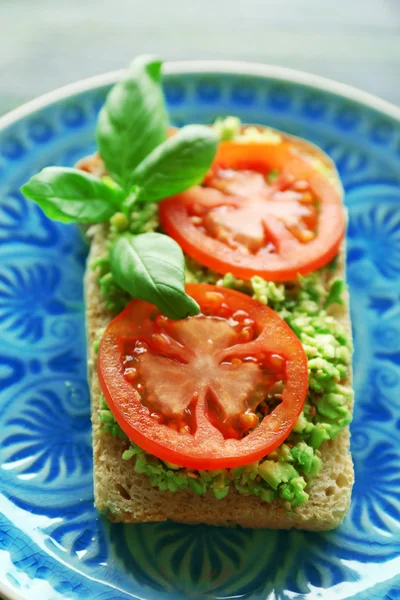 Vegan sandwich with avocado and vegetables on plate, on wooden background