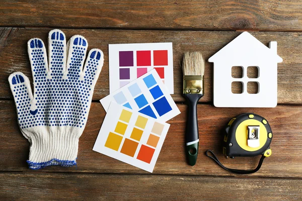 Color samples, decorative house, gloves and paintbrushes on wooden table background — Stock Photo, Image