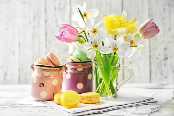 Buquê de primavera em caneca de vidro e saborosos macaroons na cor de fundo de madeira — Fotografia de Stock