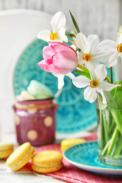 Bouquet de printemps en tasse en verre et macarons savoureux sur fond de bois de couleur — Photo