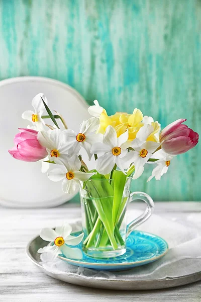 Frühlingsstrauß im Glasbecher auf farbigem Holzhintergrund — Stockfoto