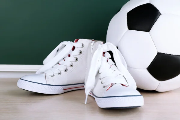 Sport shoes and soccer ball on blackboard background — Stock Photo, Image