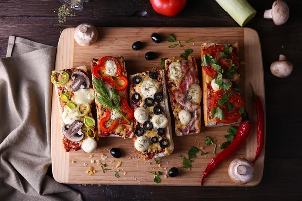 Sanduíches diferentes com legumes e queijo na tábua de corte na mesa de perto — Fotografia de Stock