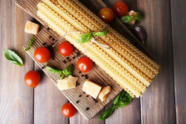 Raw pasta with cheese and vegetables on wooden background — Stock Photo, Image