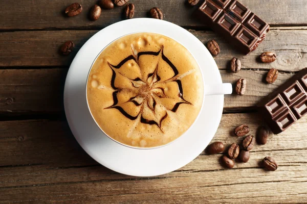 Xícara de café arte latte com grãos e chocolate na mesa de madeira, vista superior — Fotografia de Stock