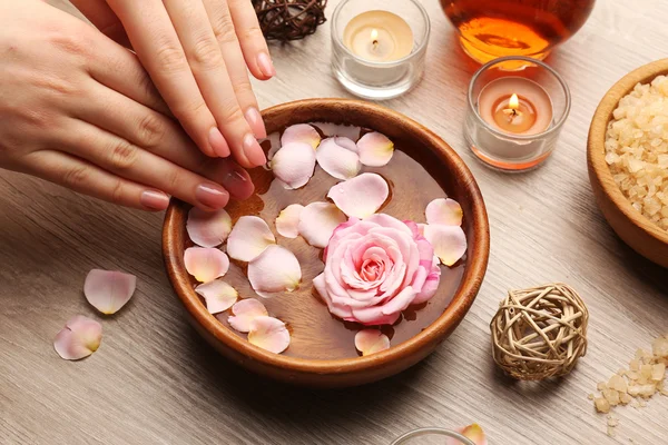 Manos femeninas y tazón de agua de spa con flores, primer plano — Foto de Stock