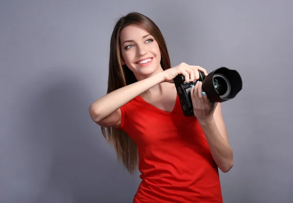 Young female photographer taking photos on grey background