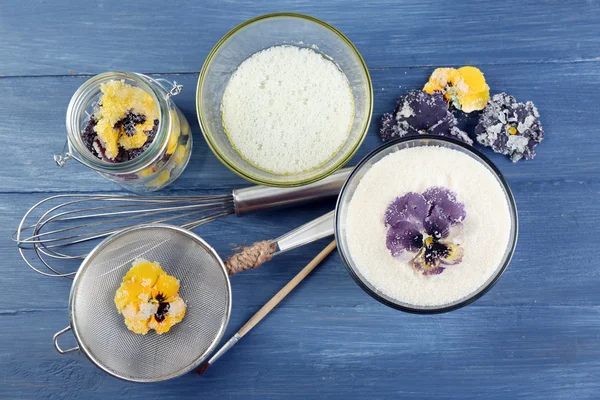 Elaboración de flores violetas confitadas con claras de huevo y azúcar, sobre fondo de madera de color — Foto de Stock