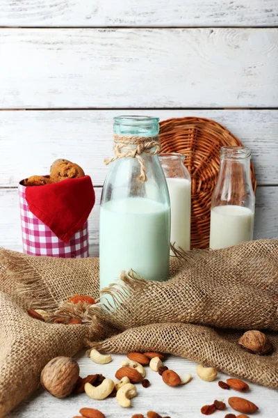 Milk in glassware and walnuts on wooden table with sackcloth, closeup — Stock Photo, Image