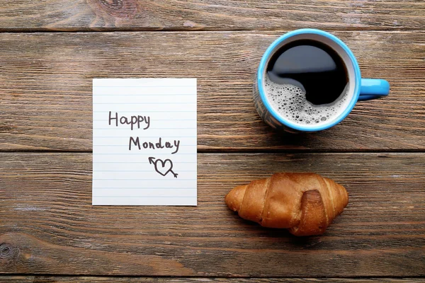 Kopp kaffe med färsk croissant och glad måndag massage på träbord, ovanifrån — Stockfoto