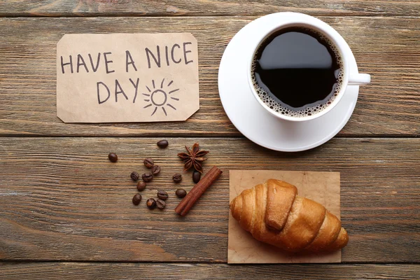 Tasse Kaffee mit frischem Croissant und eine schöne Tagemassage auf Holztisch, Blick von oben — Stockfoto