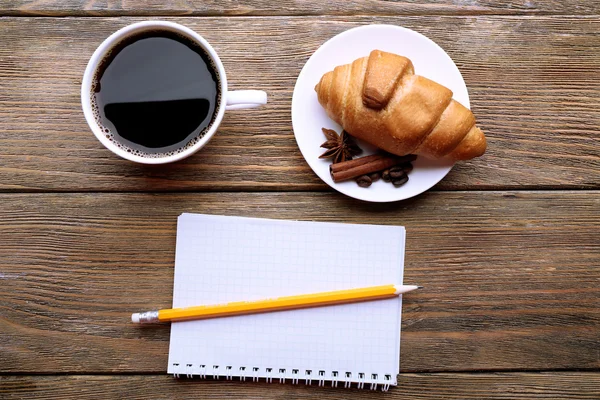 Tasse de café avec croissant frais et feuille de papier vierge sur table en bois, vue sur le dessus — Photo