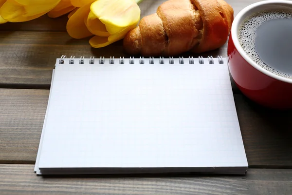 Kopje koffie met verse croissants, tulpen en blanco vel papier op houten achtergrond — Stockfoto