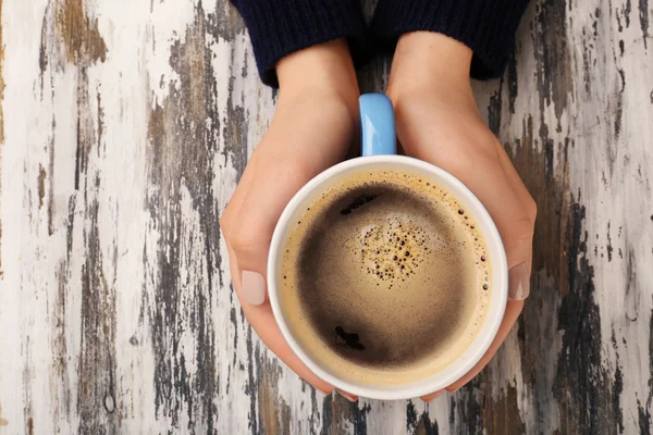 Weibliche Hände mit einer Tasse Kaffee auf hölzernem Hintergrund — Stockfoto